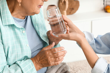 Senior woman drinking water with her granddaughter in kitchen, closeup