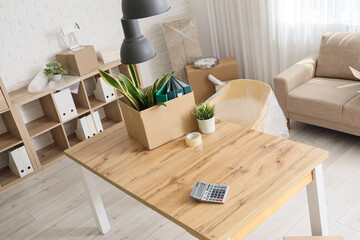 Desk with cardboard box and plants in office on moving day