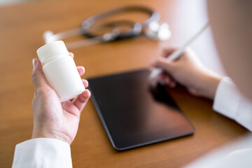Doctor holding medicine bottle and writing on digital tablet with stylus, representing digital prescription management, healthcare technology, and accurate medical documentation in a clinical.