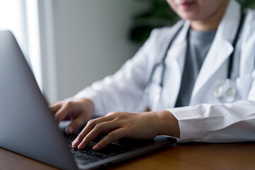 Doctor wearing white coat and stethoscope typing on laptop in clinical. Digital healthcare, electronic patient records, telemedicine and modern data management in medical practice.
