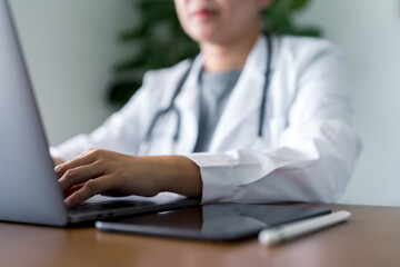 Medical professional in white coat working on laptop with digital tablet and stylus nearby, representing digital healthcare, telemedicine, and efficient electronic documentation in clinical practice.