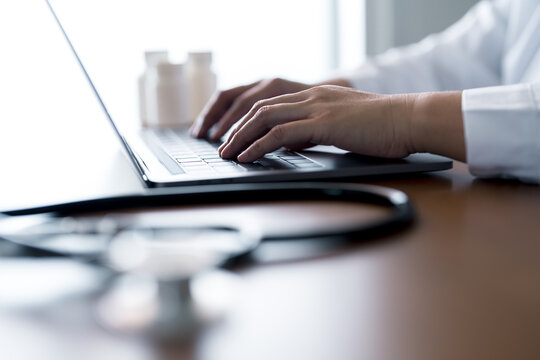 Doctor using laptop with stethoscope and medicine bottles on desk, representing digital healthcare, online patient management, e-prescriptions and electronic health record systems in modern medical.