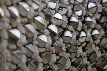 close-up of a textured surface covered in numerous small, silver, semi-circular mirrors embedded in a grey material.