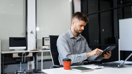 A smart Caucasian businessman sits confidently at desk in modern indoor office, using laptop for online consulting, showcasing professionalism, success, digital expertise in corporate environment.