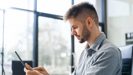 A smart Caucasian businessman sits confidently at desk in modern indoor office, using laptop for...