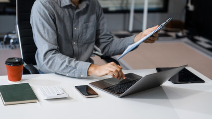 A smart Caucasian businessman sits confidently at desk in modern indoor office, using laptop for...