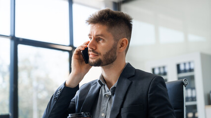 A smart Caucasian businessman sits confidently at desk in modern indoor office, using laptop for...