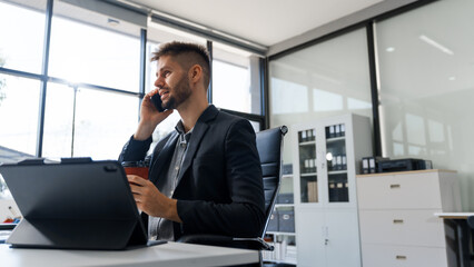 A smart Caucasian businessman sits confidently at desk in modern indoor office, using laptop for...