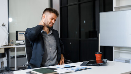 A stressed Caucasian businessman in a suit sit indoors at an office desk, suffering from office...