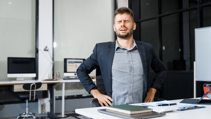 A stressed Caucasian businessman in a suit sit indoors at an office desk, suffering from office...