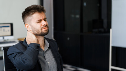 A stressed Caucasian businessman in a suit sit indoors at an office desk, suffering from office...