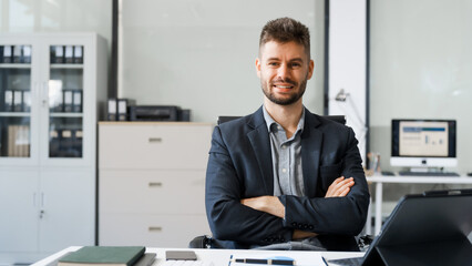 Fototapeta premium A smart Caucasian businessman sits confidently at desk in modern indoor office, using laptop for online consulting, showcasing professionalism, success, digital expertise in corporate environment.