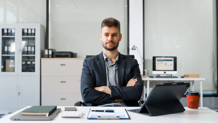 Naklejka premium A smart Caucasian businessman sits confidently at desk in modern indoor office, using laptop for online consulting, showcasing professionalism, success, digital expertise in corporate environment.