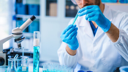 Young Caucasian male scientist works in laboratory, analyzing chemical samples with glassware and...