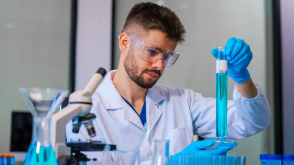 Young Caucasian male scientist works in laboratory, analyzing chemical samples with glassware and...