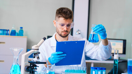 Young Caucasian male scientist works in laboratory, analyzing chemical samples with glassware and...