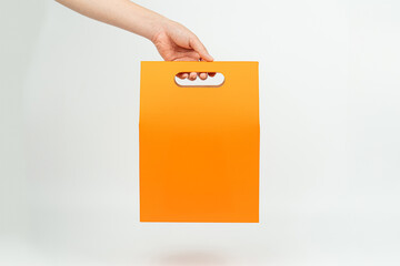 Hand holding orange paper shopping bag on white background