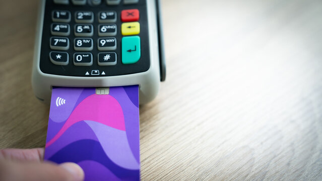 A person is using a credit card to pay for something. The card has a purple and blue design