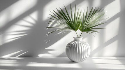 Minimalist image of fan palm leaves in a white ceramic vase, dramatic light streaming from above left, casting defined, spiky shadows on both wall and tabletop. Earth-toned interior.