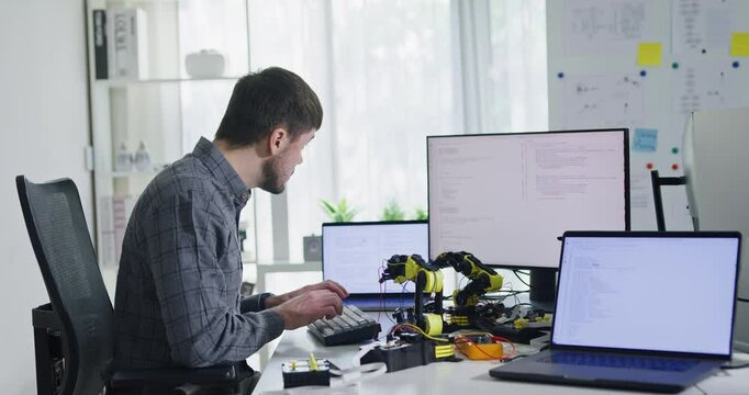Portrait confident smiling male programmer working with robotics code AI software and looking at camera in tech office. Artificial intelligence dashboard, robotics, user interface, machine learning.