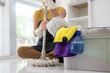 A woman is sitting on the floor with a mop and bucket in front of her. She is wearing an apron and...