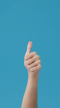 Vertical Screen : Young woman hand showing thumb up sign with fingers isolated over blue background in studio. Copy space for place a text, message for advertisement. Advertising area, mock up.