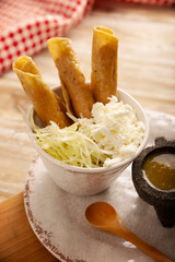 Flautas Ahogadas (Drowned Flautas) Golden tacos made with fried corn tortillas, filled with chicken or beef, and served in a glass or cup containing salsa or broth, lettuce, sour cream, and cheese.