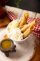 Flautas Ahogadas (Drowned Flautas) Golden tacos made with fried corn tortillas, filled with chicken or beef, and served in a glass or cup containing salsa or broth, lettuce, sour cream, and cheese.