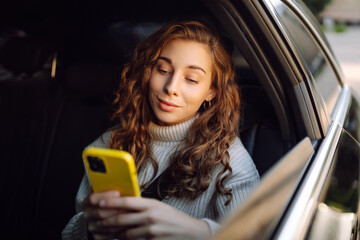 Young woman with phone sitting on back seat of car looking out window. Happy woman in taxi texting...