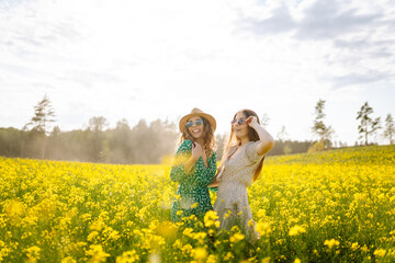 Two young female friends having fun in a yellow rapeseed field, enjoying a walk. Beautiful women...
