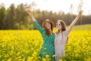 Two young female friends having fun in a yellow rapeseed field, enjoying a walk. Beautiful women...