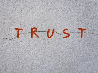 Gray wall with text written TRUST on crack - means trust is broken - when someone we trust break expectations or promises made within relationship - Betrayal leading to insecurity and emotional pain.