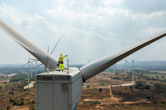 Electric engineer wearing Personal protective equipment working on top of wind turbine farm.