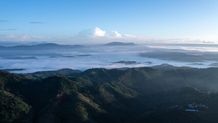 Obraz premium wide-angle view of vast morning mountain scenery with a sea of mist covering the valleys below, contrasting with the blue sky and soft sunlight, depicting the grandeur and tranquility of nature.