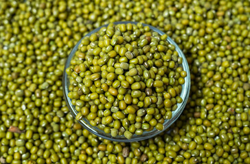 Top shot of green Moong dal beans in a glass bowl isolated on a green background. The mung bean or...