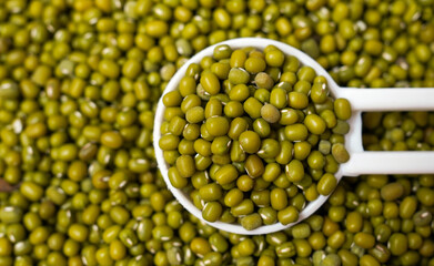 Macro close-up of organic green gram (Vigna radiata) or whole green moong dal on a white ceramic soup spoon. Top view, over gradient background of itself.
