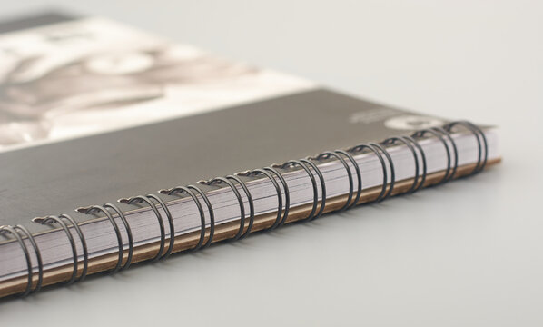 close-up of black metal spiral binding of notebook or sketchpad on gray surface, side view taken in soft focus with copy space