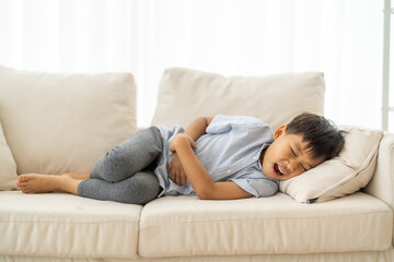 Portrait of sick unhappy little child asian boy touching belly stomach with suffering from stomach...