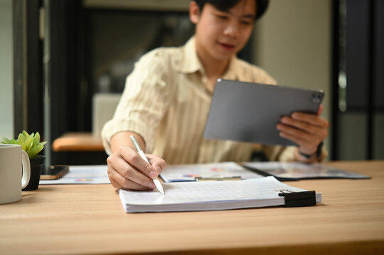 Close-up of an auditor analyzing financial documents while reviewing data on a digital tablet - Powered by Adobe