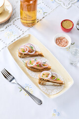 Herring toasts with onion, bright natural lighting, overhead composition on embroidered tablecloth
