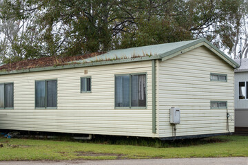 A neglected cabin in an old holiday park or caravan site in Australia with weeds growing in the roof gutter and grime on the siding.