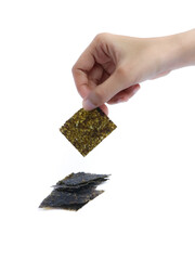 A hand picking up a square piece of dried seaweed snack with a stack of seaweed sheets on a white background, isolated for commercial food presentation or packaging use.