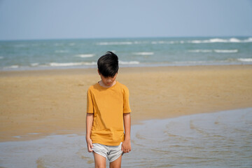 Asian boy in orange t-shirt walks along the beach during long holiday,idea of ​​using sea waves as a therapy
