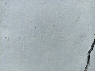 White Wall with Vertical Crack and Subtle Texture. Close-up of a white painted wall featuring subtle texture and a prominent vertical crack on the right, ideal for backgrounds or design overlays