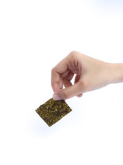 Hand holding a square sheet of roasted seaweed snack against a white background.