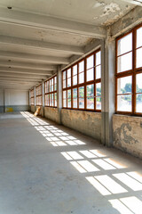 Abandoned industrial hall with old furniture, metal parts, and dusty workspaces. Atmospheric lost place showing decay, machinery remnants, and natural light through large windows.