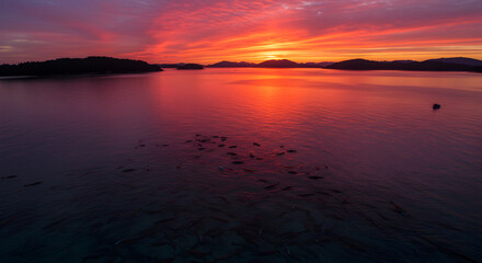 Stunning sunset landscape over a tranquil lake with dark silhouettes of mountains