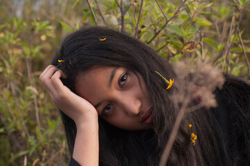 Sad young woman resting head on hand outdoors with yellow flowers in hair