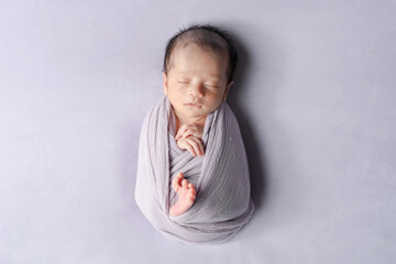 A professional newborn photo of a two-week-old Japanese baby, peacefully sleeping while wrapped in...
