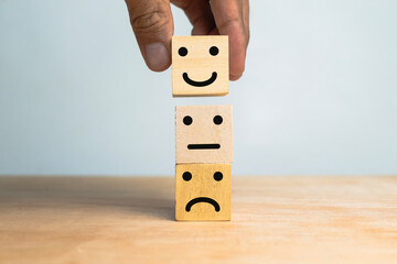 male hand stack sad, flat and happy face expression emoticon on wooden cubes on wooden table